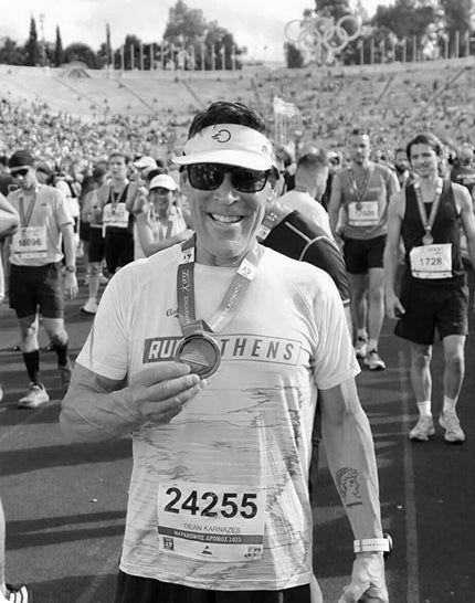 Dean holding a medal at a marathon with other runners in the background