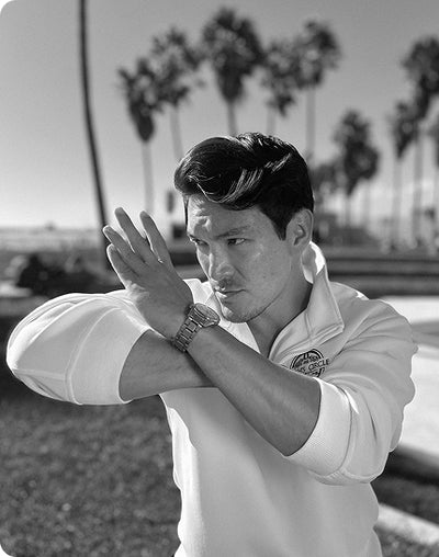 Noah in a white shirt with a logo, standing outdoors with palm trees in the background