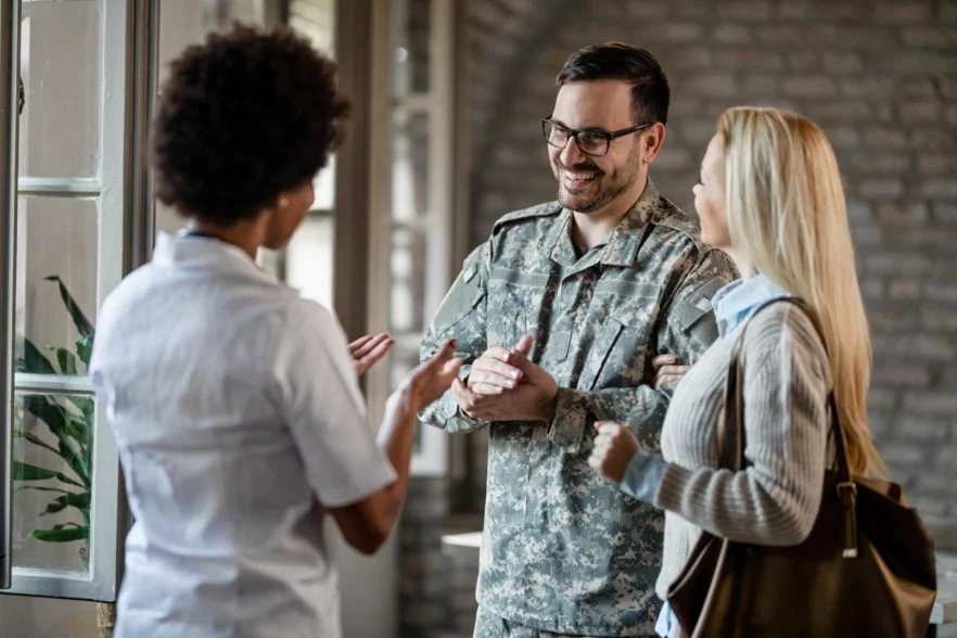 happy army soldier and his wife communicating with african american healthcare worker while having consultations at the clinic