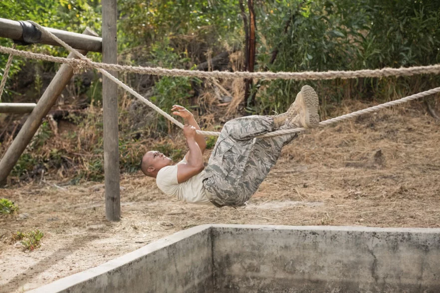 military soldier climbing rope during obstacle course training at boot camp
